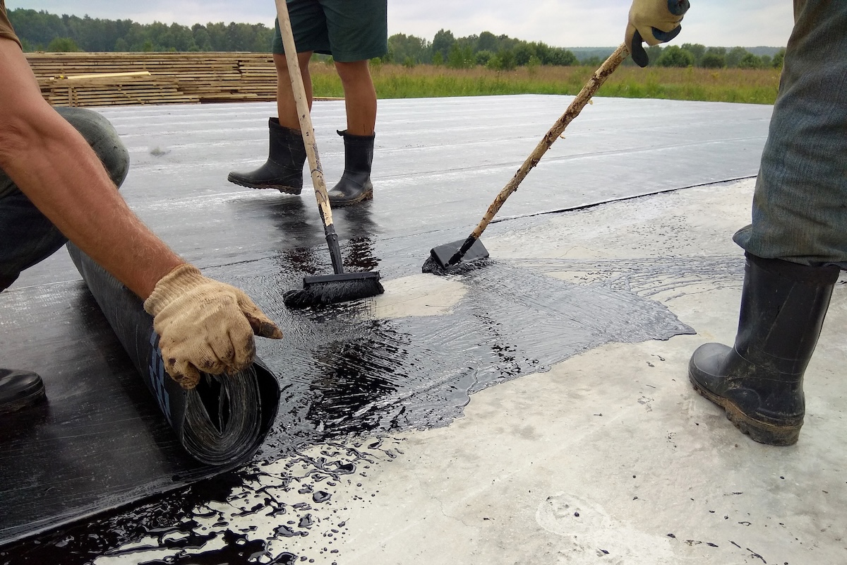 Roofer worker painting bitumen praimer at concrete surface by the roller brush