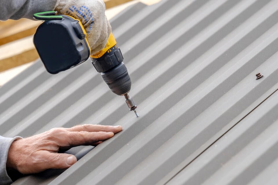 metal roof installation-close up of roofer using power drill to install panels of metal roofing on a house roof
