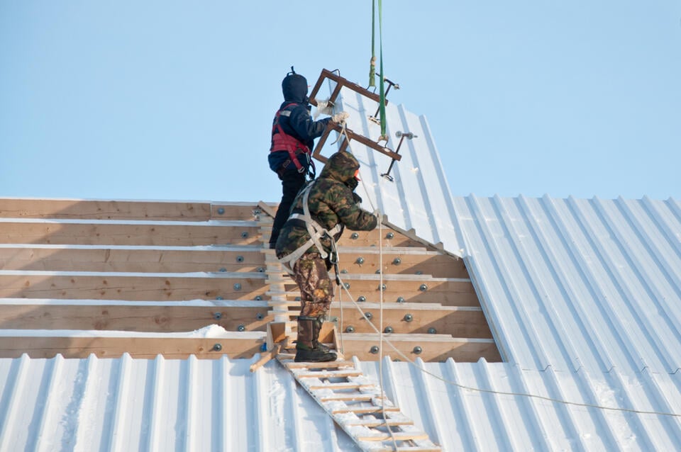 metal roof installation-two roofers installing a metal panel on a house roof with the help of a crane